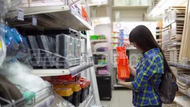 一个年轻的女人在一家建筑超市里选择了一个小橙色的容器。